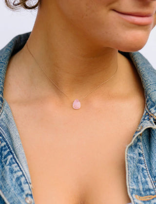 Close-up of a person wearing a delicate necklace with a pink pendant.