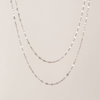 Two silver chain necklaces on a beige background