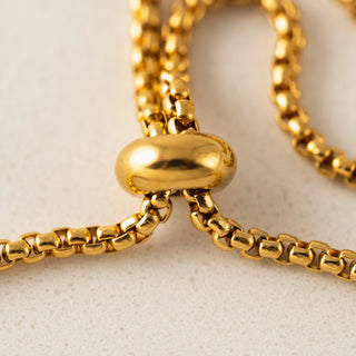Close-up of a gold chain with a unique clasp on a light beige background