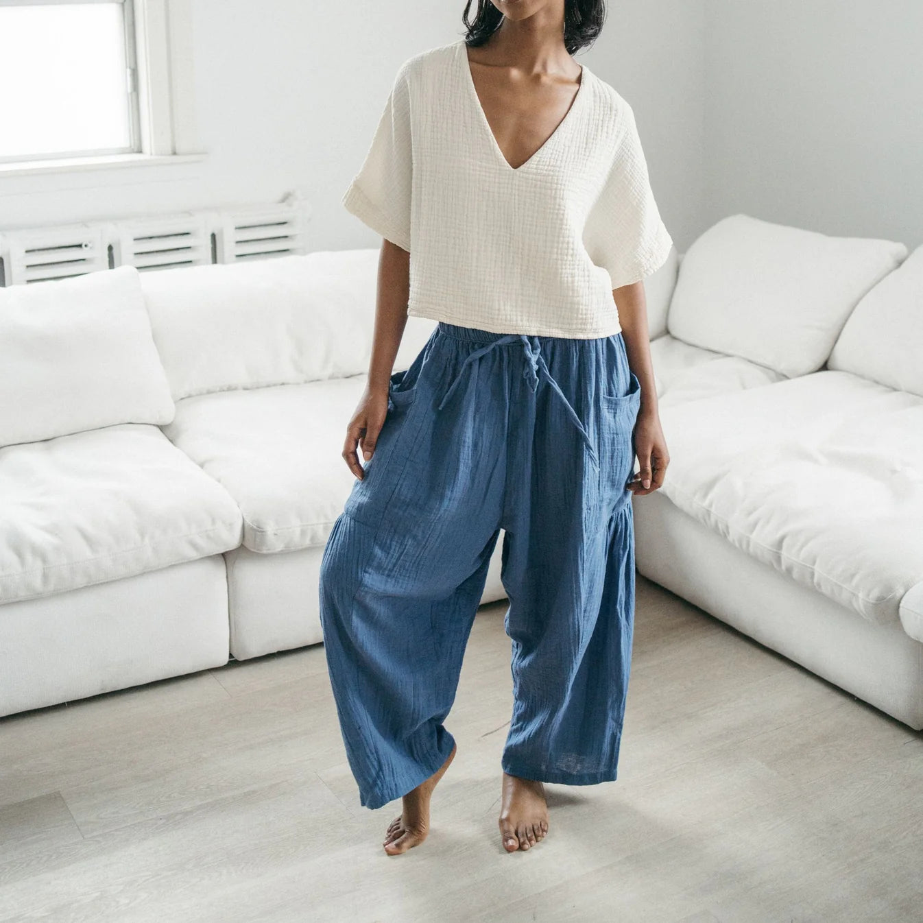 Person wearing a white top and blue pants standing in a minimalistic living room.