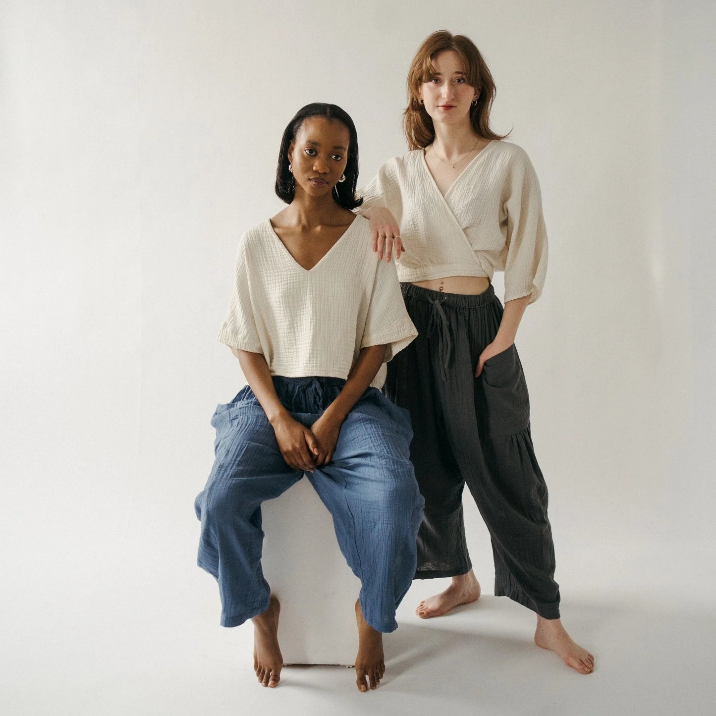 Two women sitting on a white box against a plain background