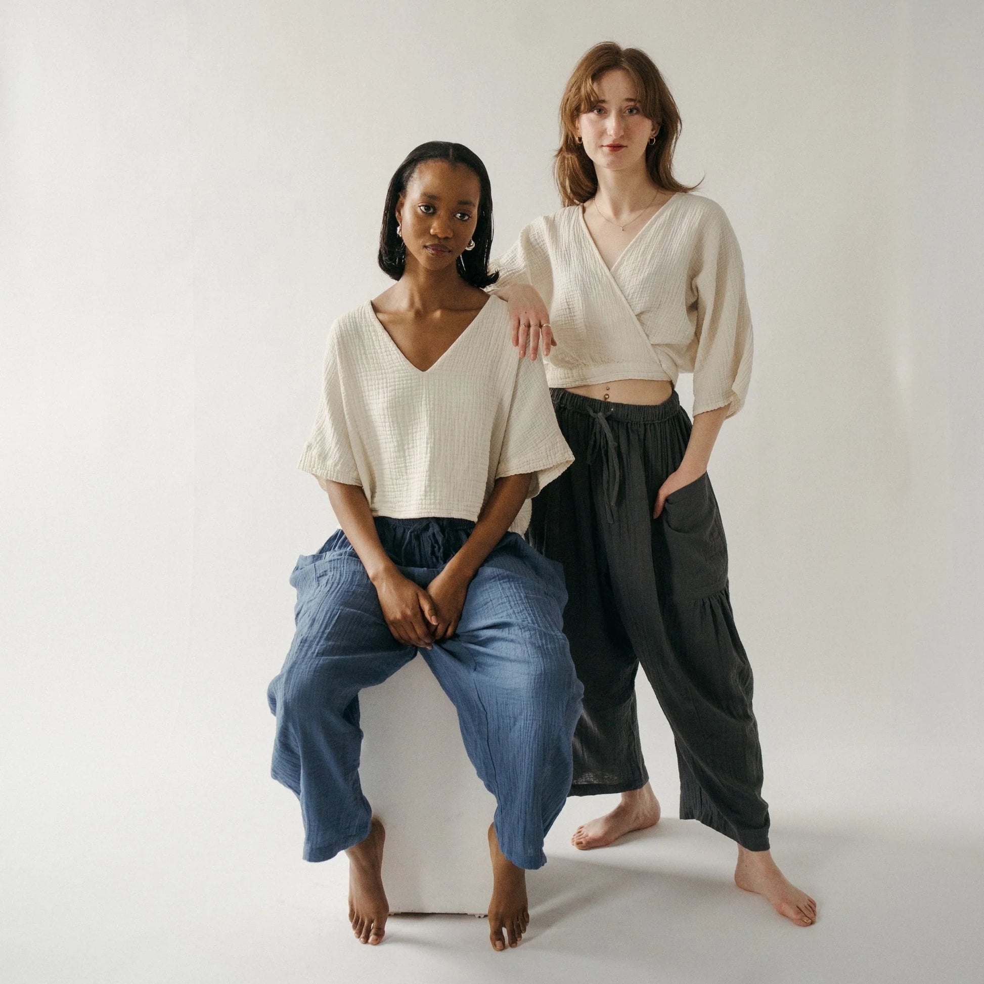 Two women sitting on a white box against a plain background