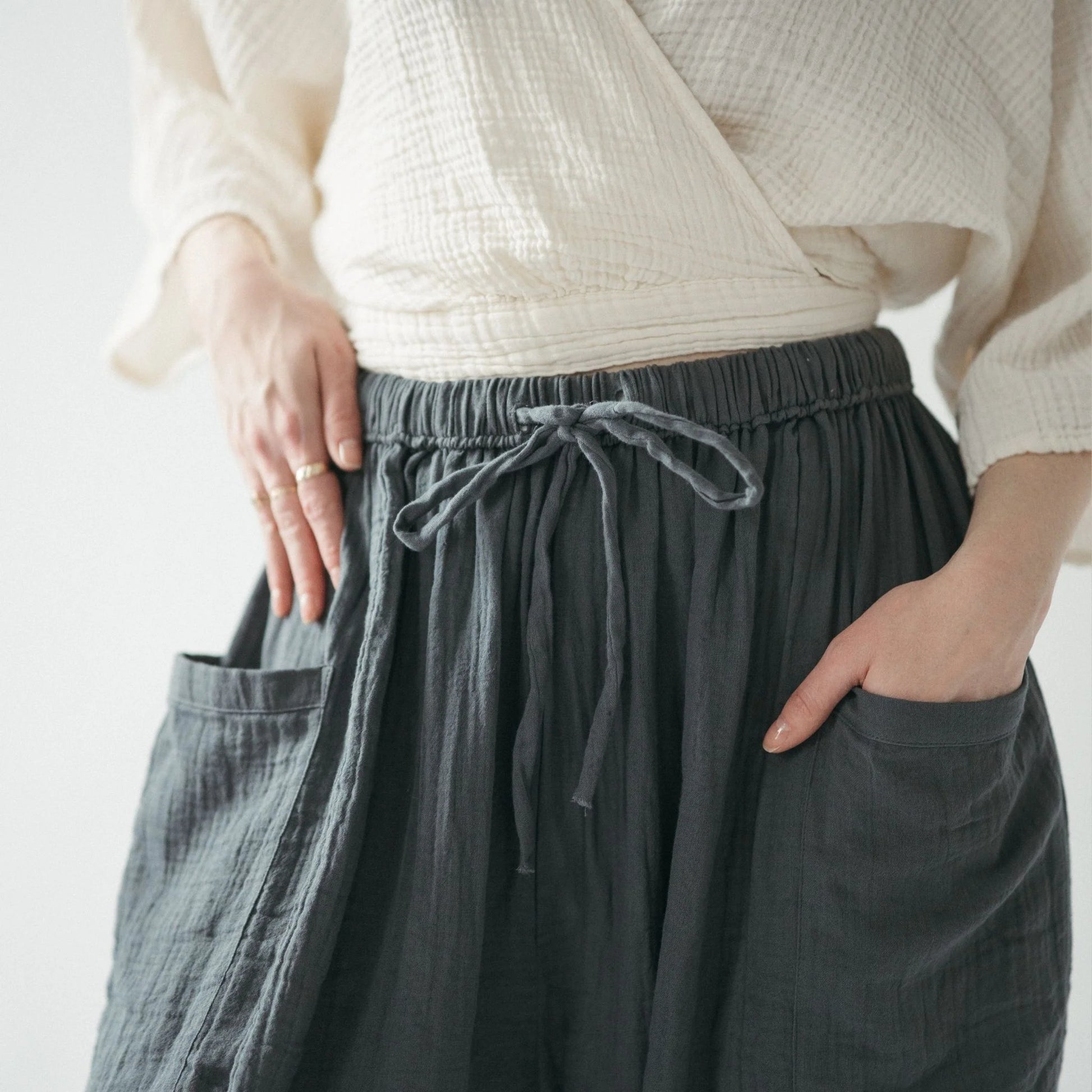 Person wearing a cream sweater and dark gray pants with a drawstring, on a light background