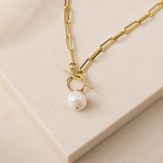 A gold-plated brass curb chain necklace with a central freshwater pearl, displayed on a white surface.