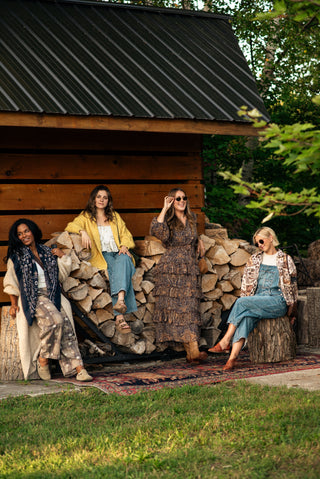 four women dressed in boho inspired clothing sitting outside an old sugar shack. 