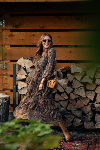 women wearing a paisley printed dress standing in front of a barn. 