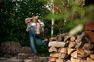 women wearing a boho printed jacket and overalls standing on logs in front of a barn. 
