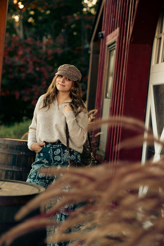a women wearing paisley printed pants and a polo style sweaters standing in front of a barn. 