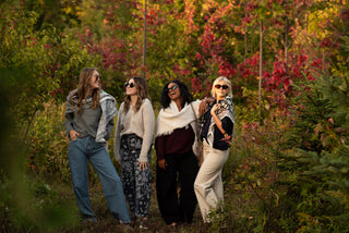 Four women in sweaters and scarves in a fall forrest. 