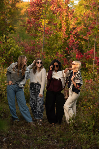 Four women in sweaters and scarves in a fall forrest. 
