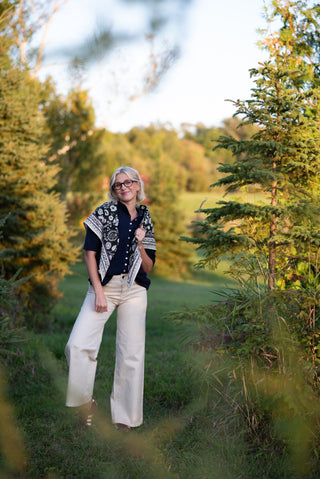 women wearing a blue cardigan, cream jeans and a printed scarf over her shoulders in a field of grass. 