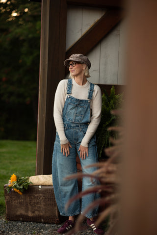 Women wearing a pair of free people overalls and a newsboy cap exiting out of a barn. 