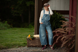 Women wearing a pair of free people overalls and a newsboy cap exiting out of a barn. 