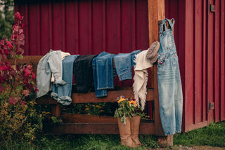 several pairs of jeans folded over and a pair of knee high boots with flowers in them in front of a barn. 