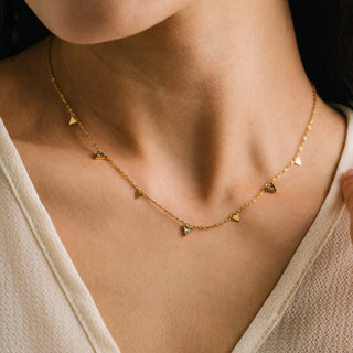 Gold necklace with small triangle pendants on a person wearing a beige top.