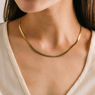 A person wearing a gold-colored herringbone chain necklace.