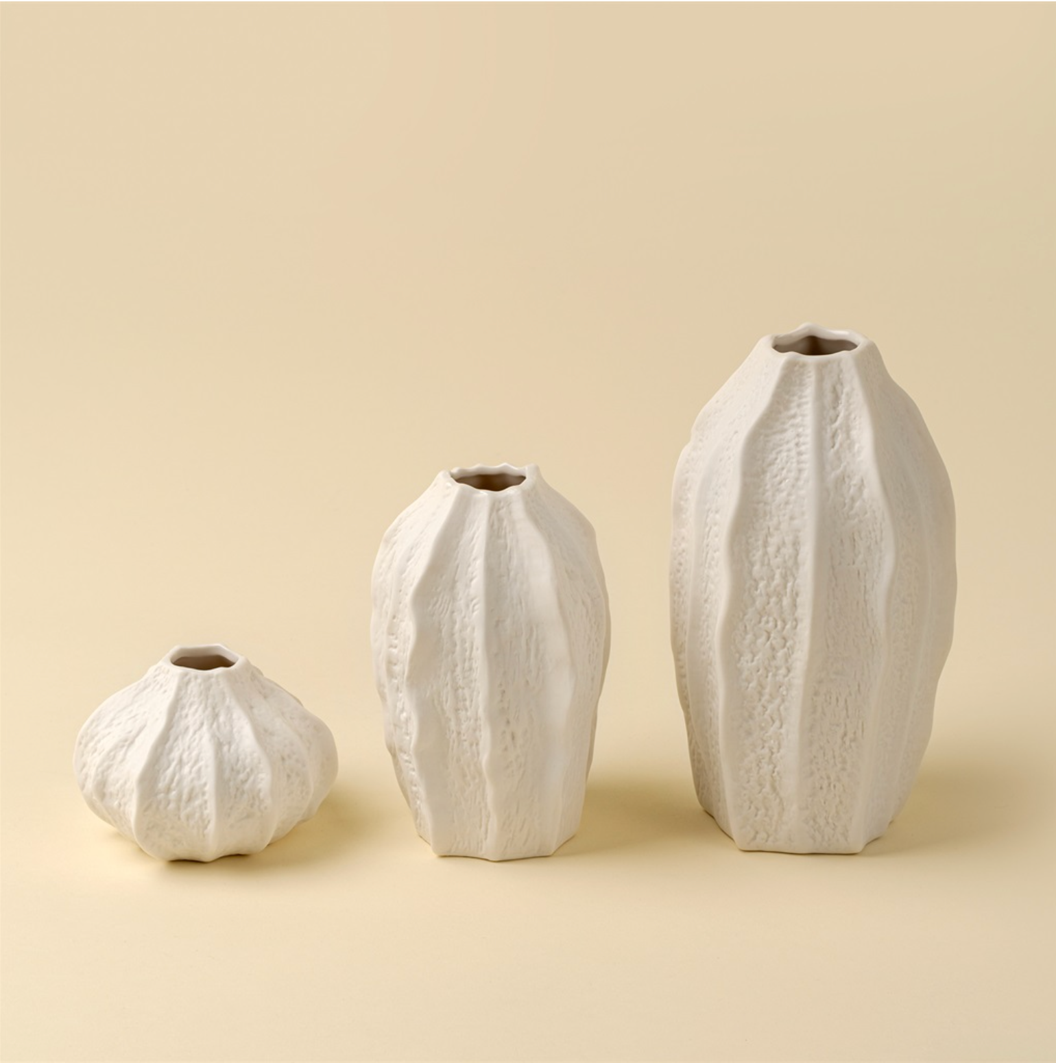 Three textured white vases of varying sizes on a beige background