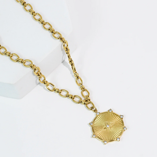 A gold pendant necklace with a sunburst design on a white background. 