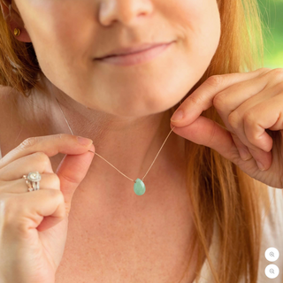 Woman adjusting a necklace with a green pendant.