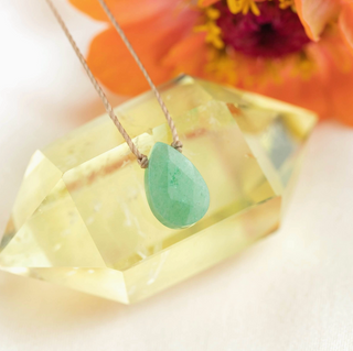 Green teardrop pendant necklace on a blurred floral background