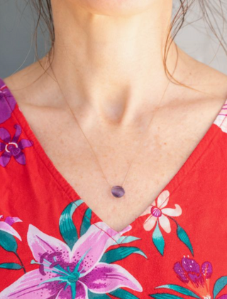 Person wearing a red floral dress with a necklace featuring a purple pendant.