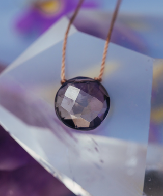 Necklace with a faceted purple gemstone pendant on a blurred background