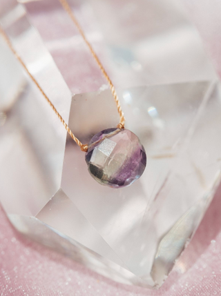 Necklace with a faceted purple gemstone pendant on a pink crystal background