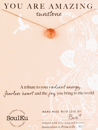 Necklace with a sunstone pendant on a beige background with text and branding.