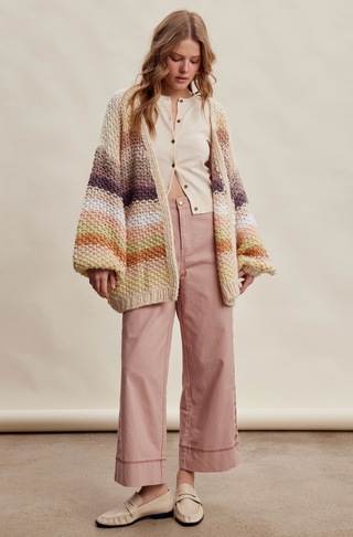 Woman wearing a striped cardigan, white shirt, and pink pants against a plain background