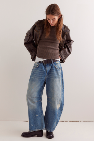 Person wearing a brown jacket, green shirt, and blue jeans against a white background