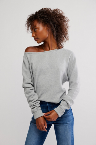 Woman wearing a gray off-shoulder sweater and blue jeans on a white background