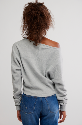 Person wearing a gray off-shoulder sweater and blue jeans on a plain background
