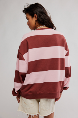 Person wearing a maroon and pink striped sweater with beige shorts on a plain background