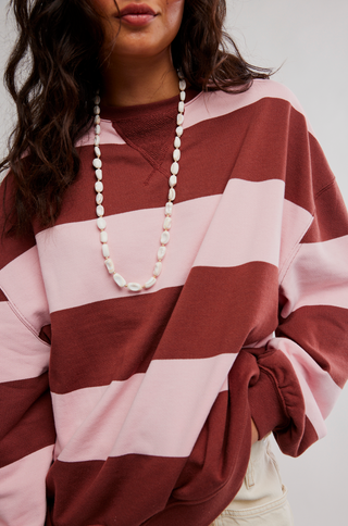 Person wearing a red and pink striped sweater with a long necklace.