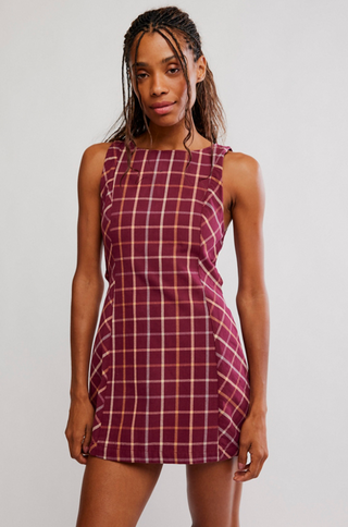 A woman modeling a sleeveless, scoop-neck mini dress with a burgundy and cream plaid pattern against a light gray studio background.