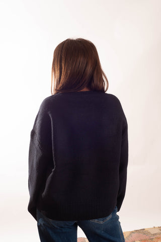 A person viewed from behind wearing an oversized dark navy knit sweater and blue jeans against a plain white studio background.