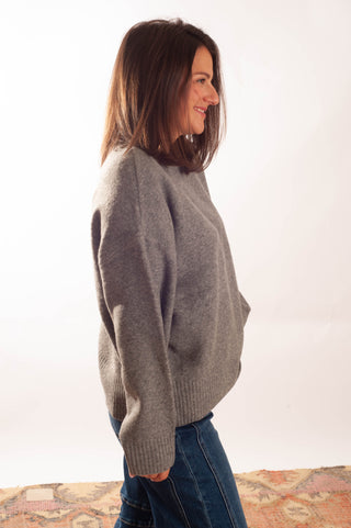 A woman wearing a gray knit crewneck sweater and blue jeans, shown in profile against a plain white background.