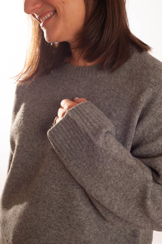 A close-up of a woman wearing a cozy, heathered dark gray knit sweater, showing the ribbed cuffs and a smile from the side of her face.