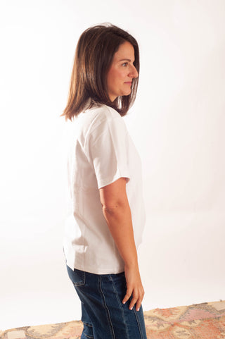 A woman with shoulder-length brown hair is shown in profile wearing a white short-sleeve t-shirt and blue jeans against a plain white studio background.