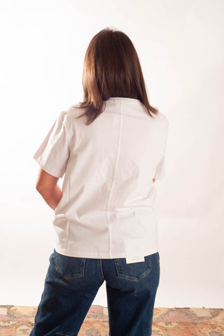 A woman viewed from behind wearing a white short-sleeve button-up shirt and blue jeans, standing against a plain white studio background.