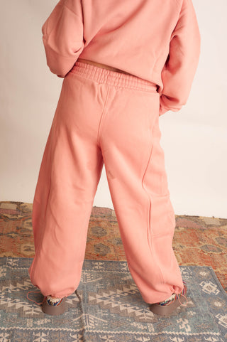A child wearing a matching dusty pink sweatshirt and jogger pants, shown from the back while standing on a patterned rug.