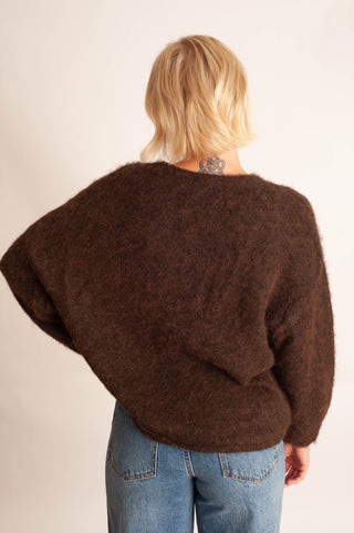 A person viewed from the back wearing a fuzzy, oversized dark brown sweater and light blue jeans against a plain off-white background.