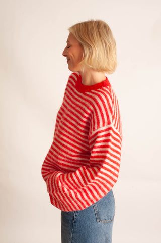 A woman with short blonde hair is shown in profile wearing a fuzzy red and white striped sweater and blue jeans against a plain light background.