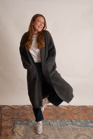 Women wearing a long charcoal cardigan against a neutral photo backdrop. 
