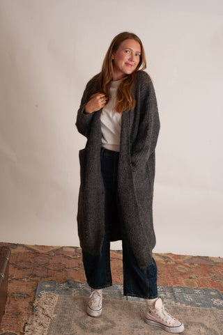 Women wearing a long charcoal cardigan against a neutral photo backdrop. 