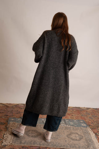 Women wearing a long charcoal cardigan against a neutral photo backdrop. 