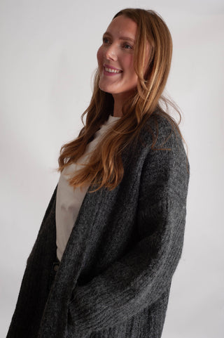Women wearing a long charcoal cardigan against a neutral photo backdrop. 