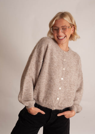 Women modelling a beige cardigan against a neutral photo background. 