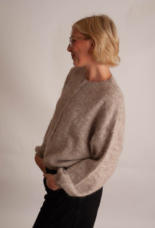 Women modelling a beige cardigan against a neutral photo background. 