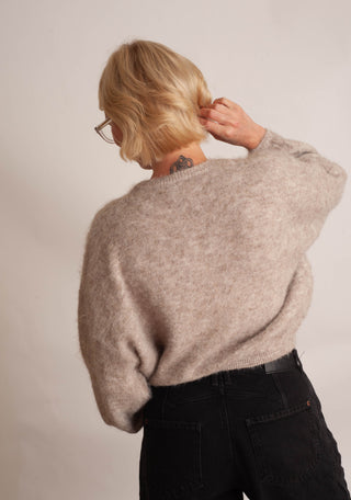 Women modelling a beige cardigan against a neutral photo background. 